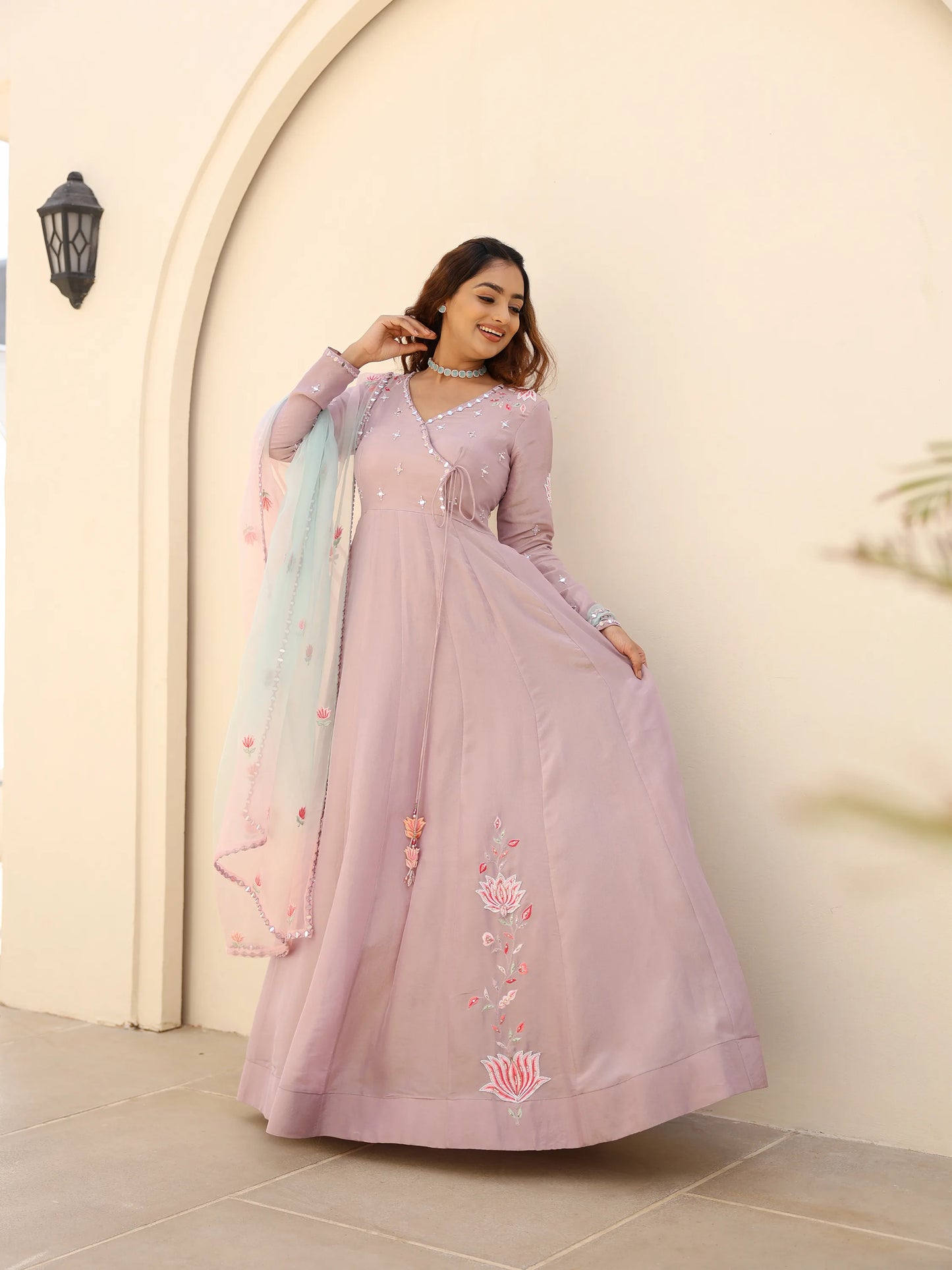 Woman in a light pink anarkali with a ombre dupatta standing against a beige wall.