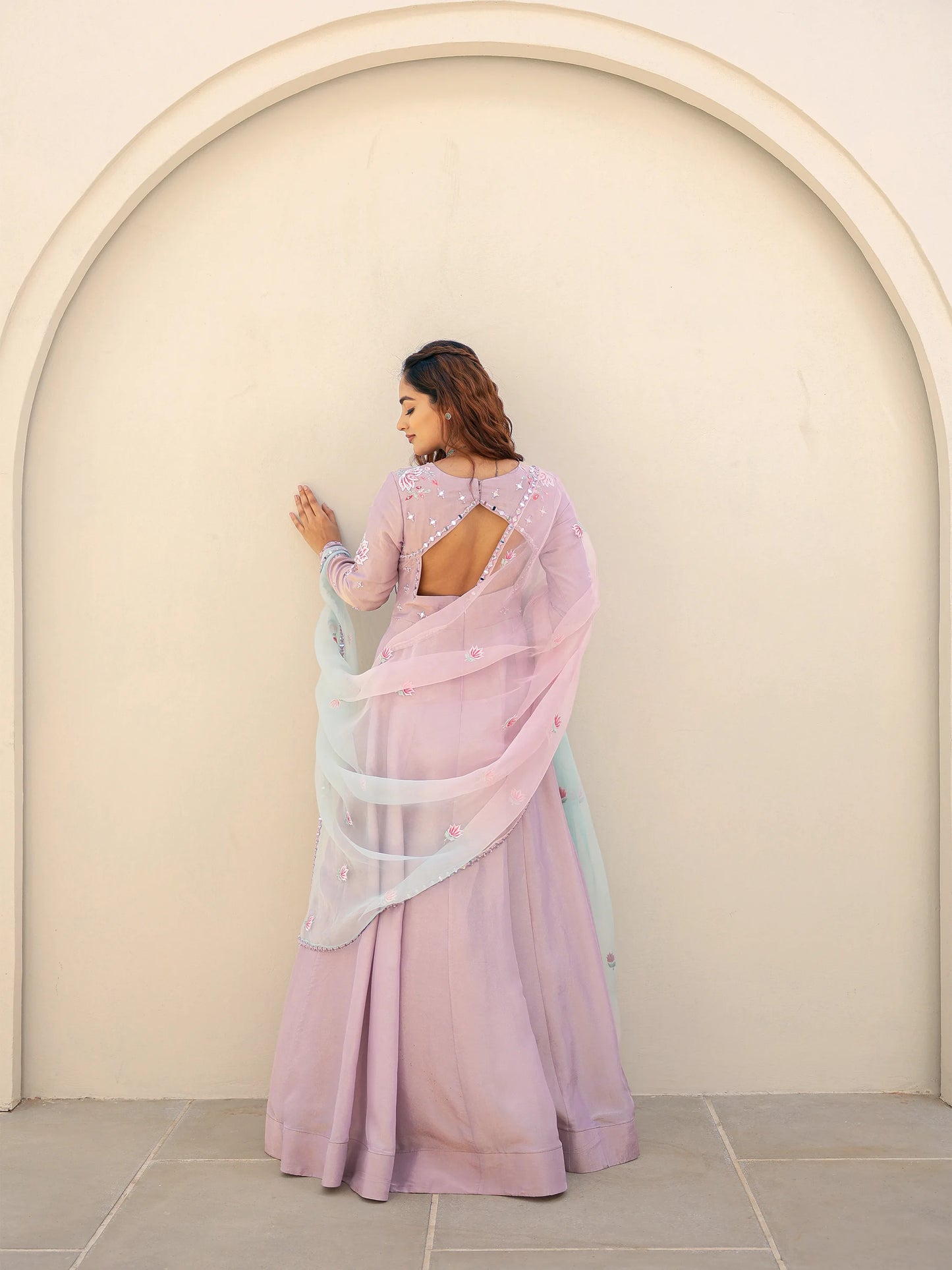 Woman in a lilac anarkali standing against a beige wall