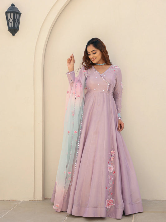 Woman wearing a lavender anarkali suit with floral embroidery in front of a beige wall.