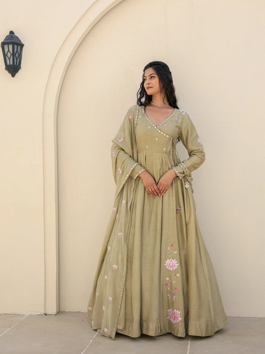 Woman wearing a sage green anarkali standing against a beige wall.