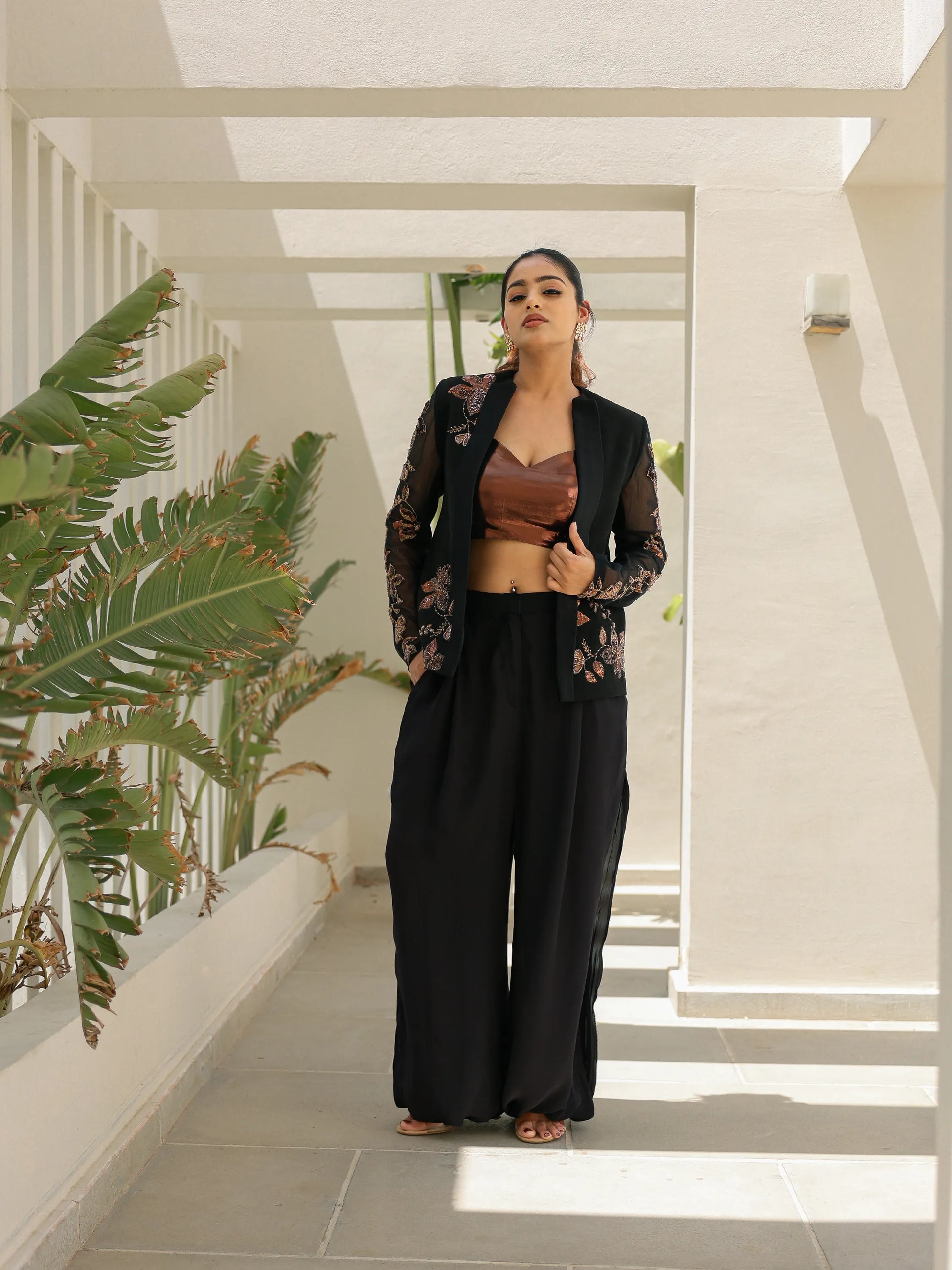 Black embroidered blazer styled with bronze crop top and wide leg pants for modern festive look.