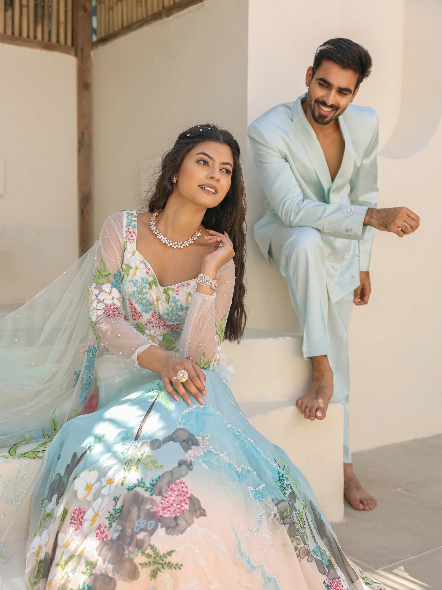 model wearing coastal ombre organza gown with tropical shoreline embroidery beside aqua silver satin linen blazer set